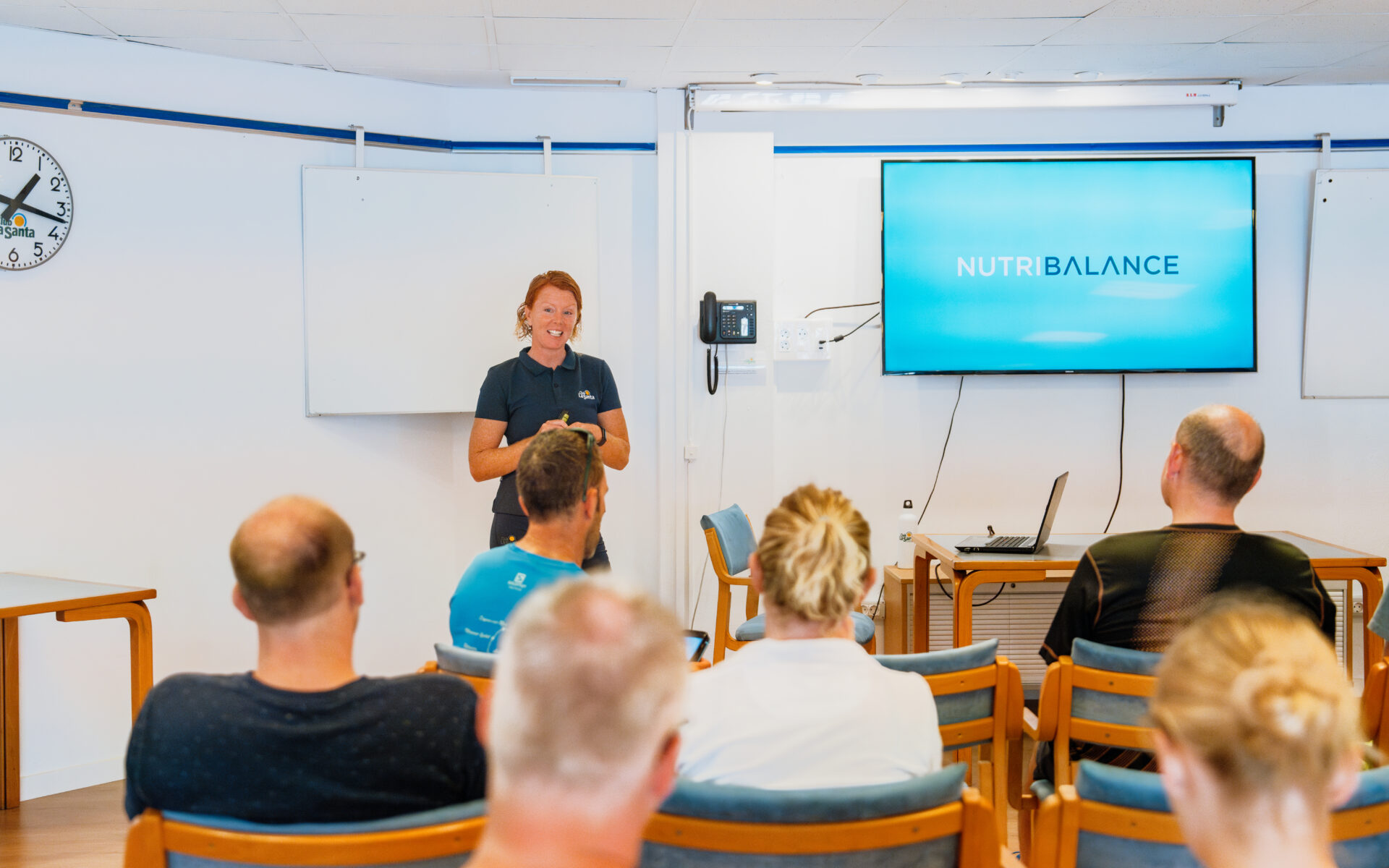 Emma Gibbins speaking to an audience of people, presenting NutriBalance on a tv screen.